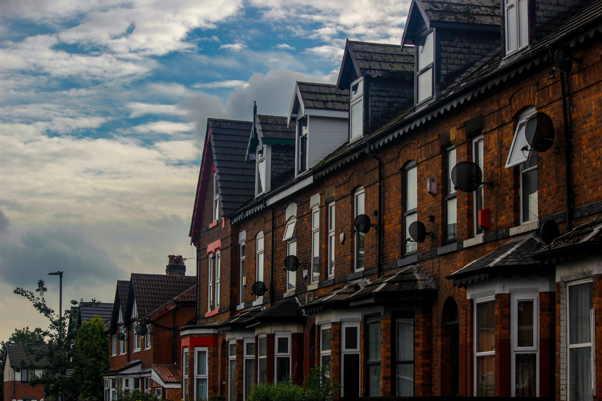 Traditional brick row houses in Manchester's suburb under a cloudy sky.